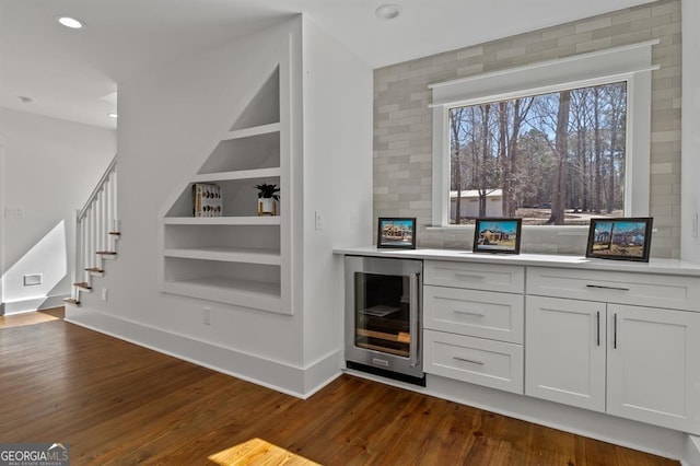 bar with built in shelves, dark wood-style flooring, stairway, beverage cooler, and baseboards