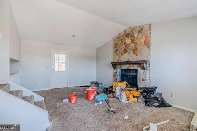 living room featuring lofted ceiling, visible vents, carpet flooring, a stone fireplace, and stairs