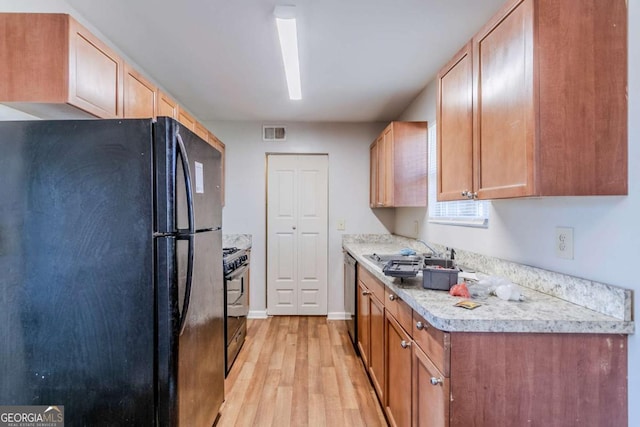 kitchen with light countertops, visible vents, a sink, light wood-type flooring, and black appliances