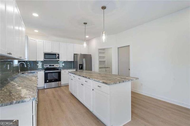 kitchen featuring stainless steel appliances, backsplash, light wood-style flooring, white cabinets, and a sink