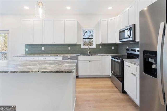 kitchen with stainless steel appliances, a sink, white cabinetry, light wood-style floors, and light stone countertops