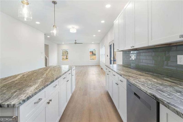 kitchen featuring pendant lighting, backsplash, light wood-style flooring, stainless steel dishwasher, and white cabinetry