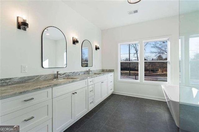 bathroom with double vanity, visible vents, a sink, a freestanding tub, and baseboards