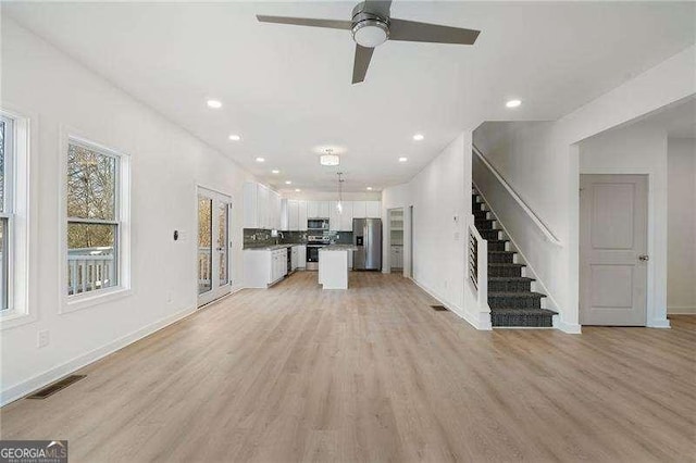 unfurnished living room featuring visible vents, baseboards, light wood-style flooring, stairs, and recessed lighting