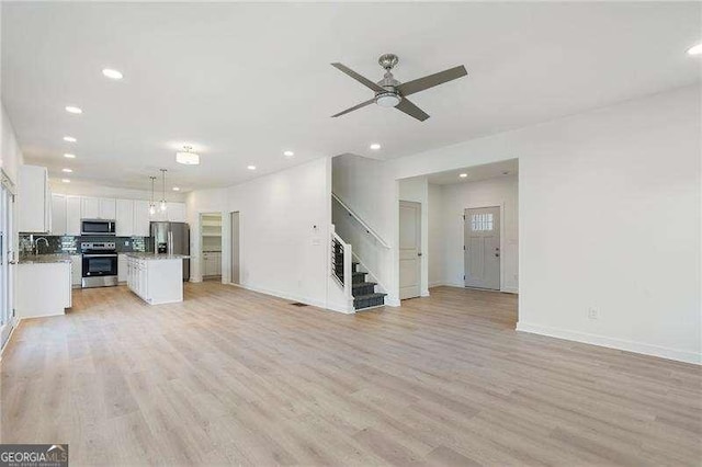 unfurnished living room with light wood-style floors, ceiling fan, baseboards, and stairs