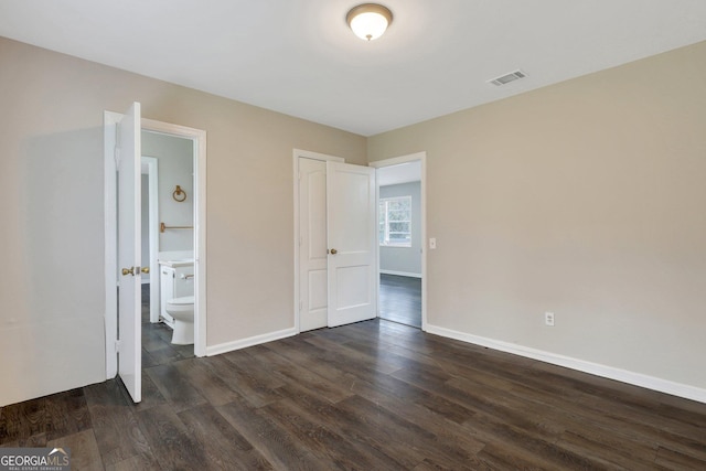 unfurnished bedroom with baseboards, visible vents, dark wood finished floors, and ensuite bathroom