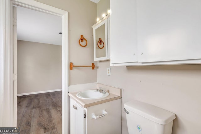 half bathroom featuring toilet, baseboards, wood finished floors, and vanity