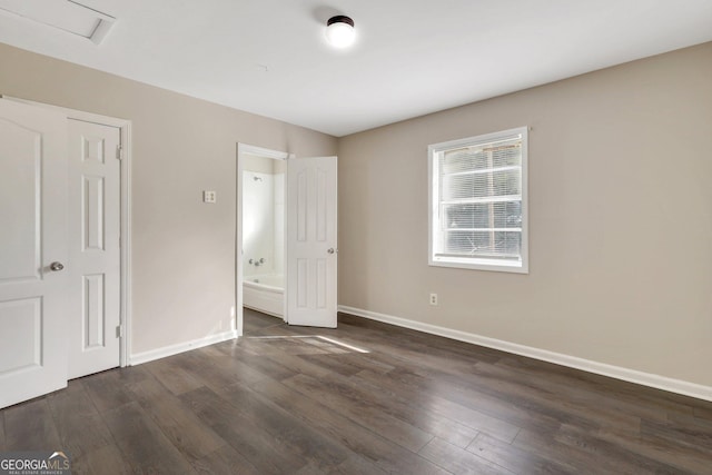 unfurnished bedroom featuring dark wood-style floors, baseboards, and connected bathroom