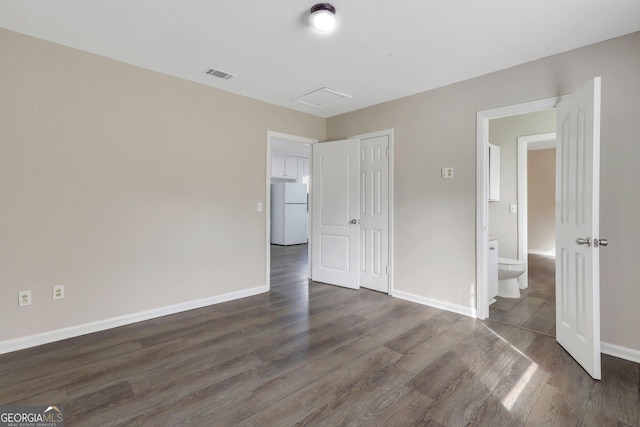 unfurnished bedroom with dark wood-style flooring, freestanding refrigerator, and baseboards