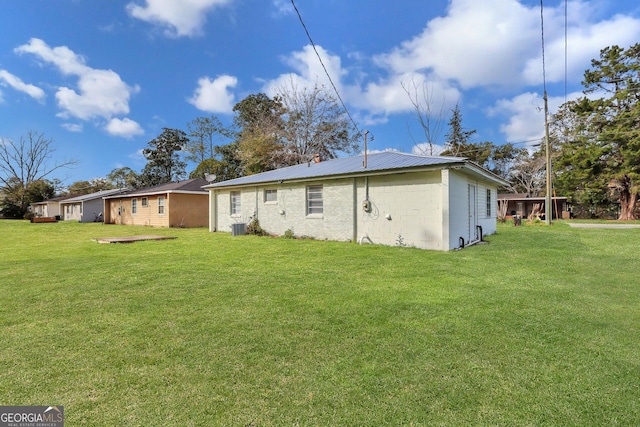 rear view of house featuring central air condition unit, metal roof, and a lawn