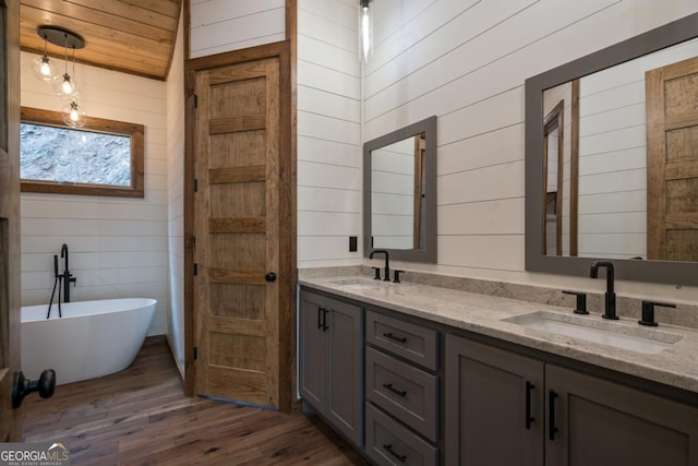 full bathroom with double vanity, a soaking tub, a sink, wooden walls, and wood finished floors