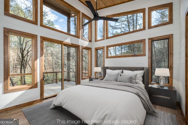 bedroom featuring a towering ceiling, access to outside, wooden walls, and wood finished floors