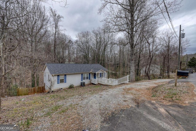 view of front facade featuring driveway, central AC unit, a forest view, and fence