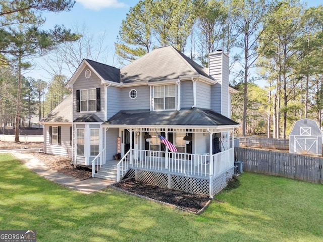 victorian-style house featuring fence, a front yard, covered porch, a chimney, and an outdoor structure