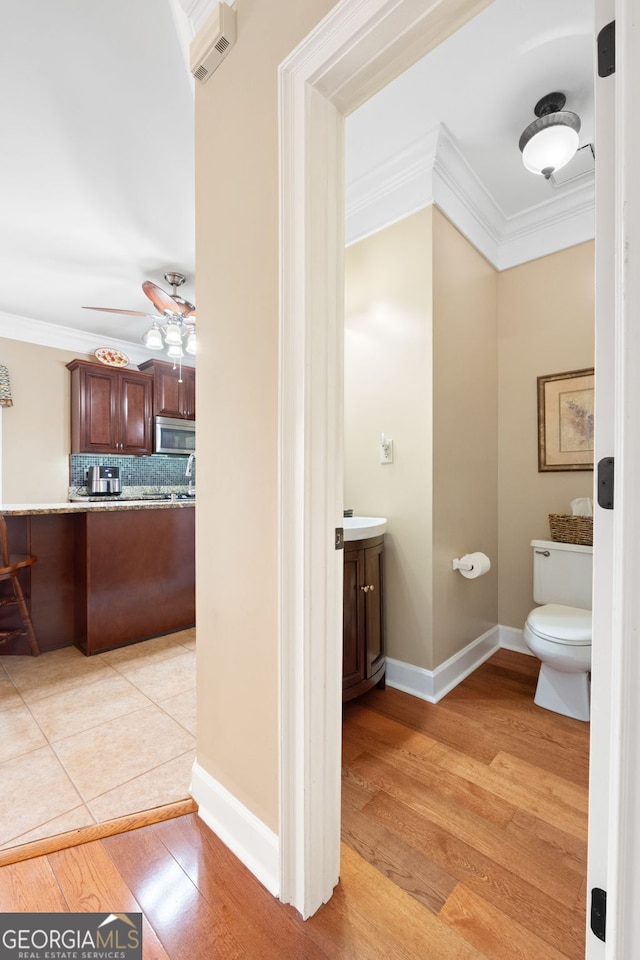 half bath featuring ceiling fan, toilet, wood finished floors, vanity, and crown molding