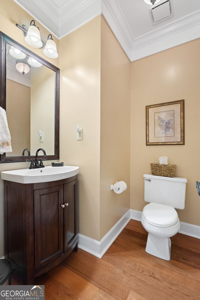 half bathroom featuring crown molding, toilet, vanity, wood finished floors, and baseboards