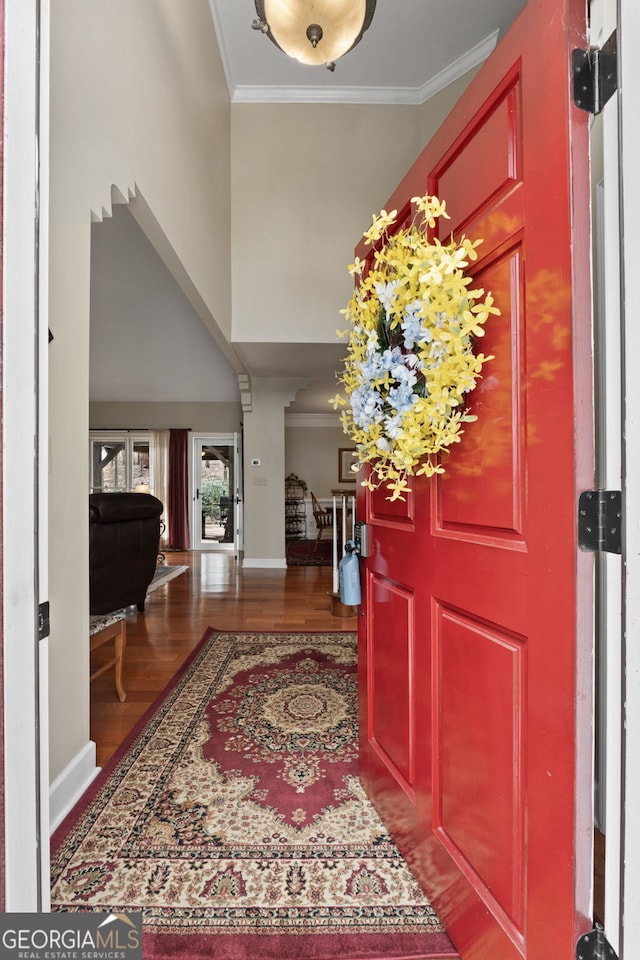 entrance foyer with ornamental molding, wood finished floors, a towering ceiling, and baseboards