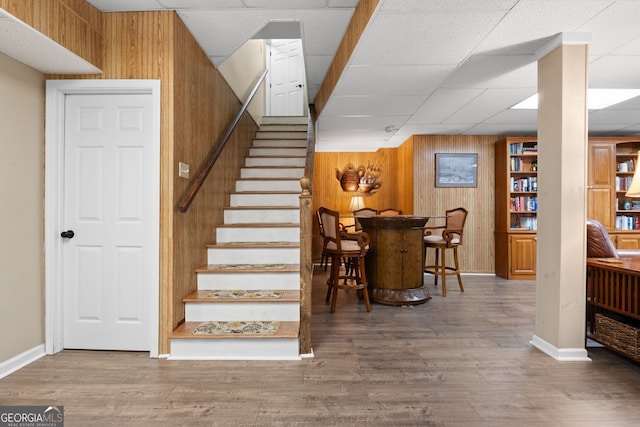 staircase featuring baseboards, wood finished floors, a paneled ceiling, and wooden walls