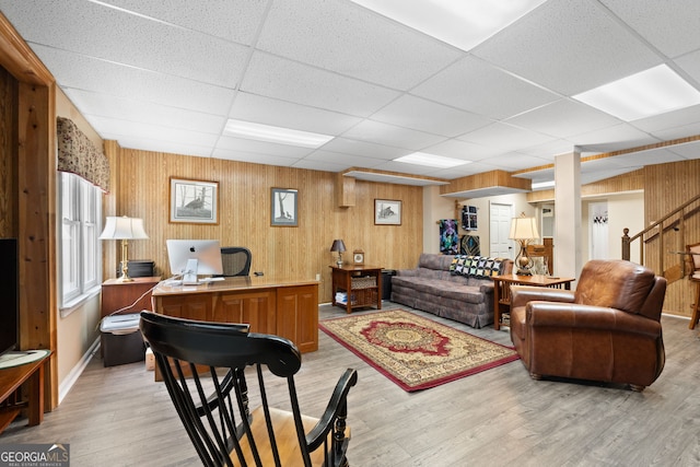 living room featuring light wood-type flooring, wood walls, baseboards, and a paneled ceiling