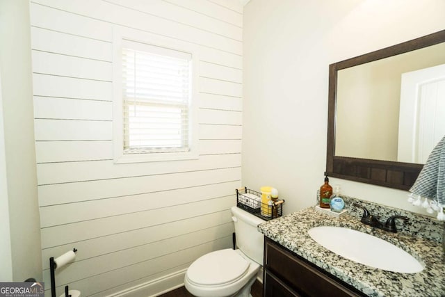 half bathroom featuring wood walls, vanity, and toilet