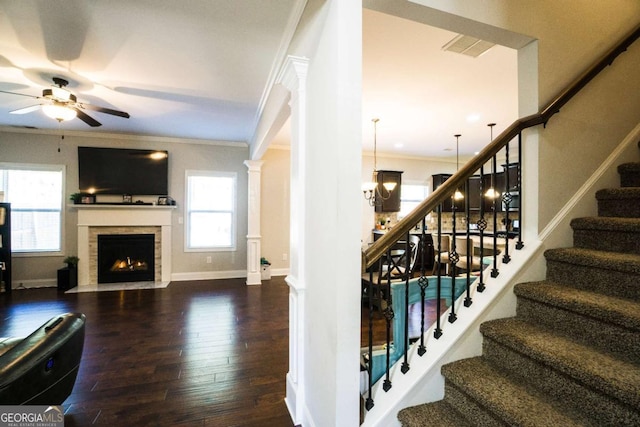 stairway featuring baseboards, a fireplace with flush hearth, wood finished floors, crown molding, and ornate columns