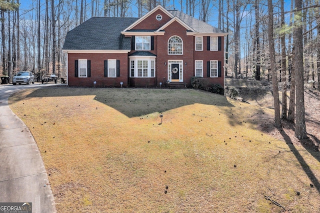 view of front facade with brick siding, roof with shingles, and a front yard