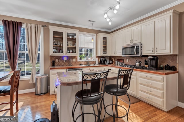 kitchen featuring light wood-style flooring, stainless steel appliances, a healthy amount of sunlight, a kitchen bar, and a sink