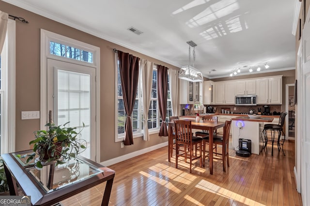 dining room featuring light wood-type flooring, baseboards, visible vents, and crown molding