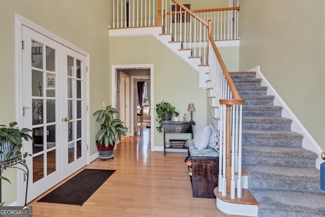 entrance foyer featuring french doors, a towering ceiling, wood finished floors, baseboards, and stairs