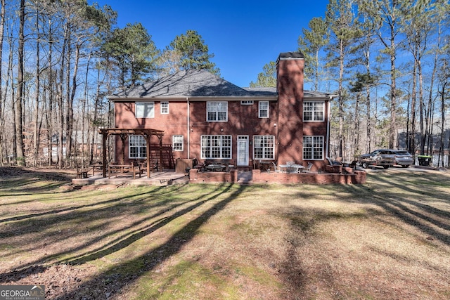 rear view of property featuring brick siding, a lawn, a pergola, a chimney, and a patio area