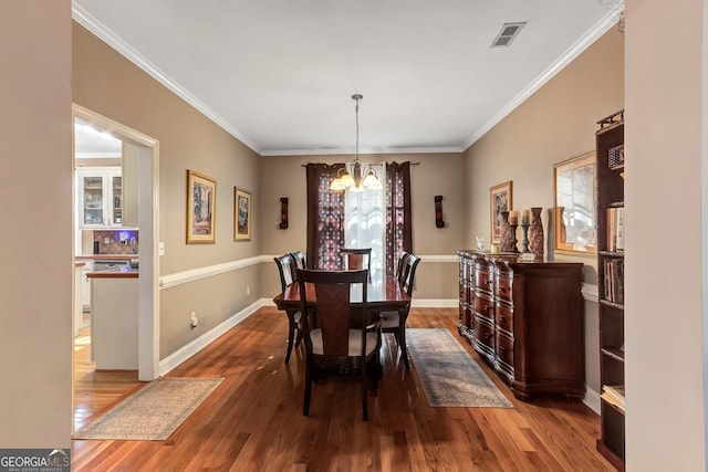 dining area featuring crown molding, visible vents, a notable chandelier, and wood finished floors