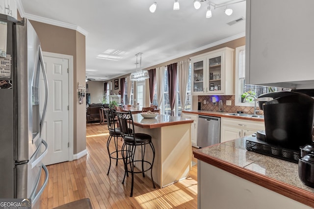 kitchen with tile counters, backsplash, appliances with stainless steel finishes, a sink, and light wood-type flooring