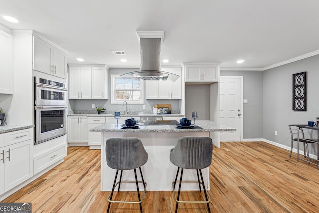 kitchen featuring light wood finished floors, double oven, a breakfast bar, and white cabinetry