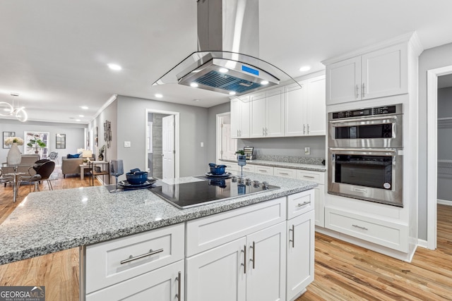 kitchen featuring island range hood, white cabinets, a center island, black electric cooktop, and double oven