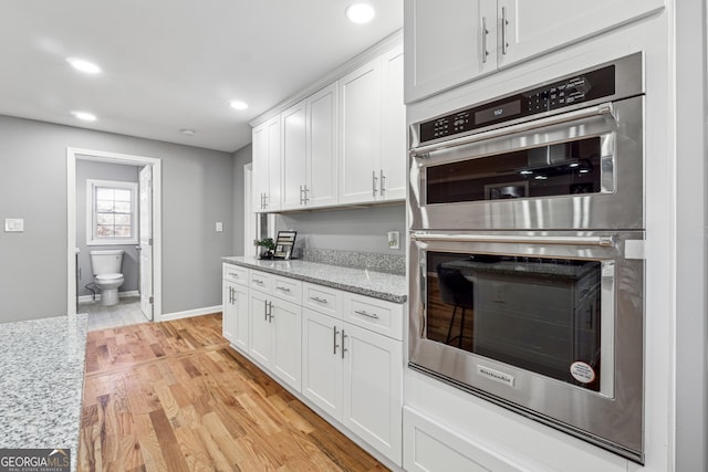 kitchen featuring stainless steel double oven, recessed lighting, white cabinetry, light wood-type flooring, and light stone countertops