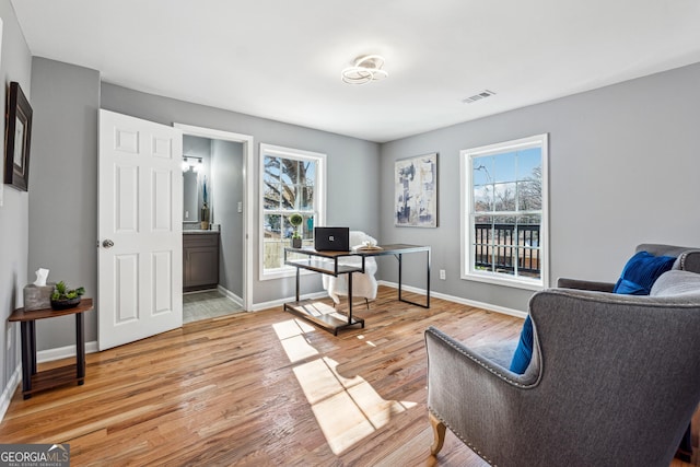 office area with plenty of natural light, light wood-style flooring, visible vents, and baseboards