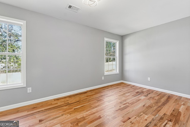 empty room with light wood finished floors, baseboards, and visible vents