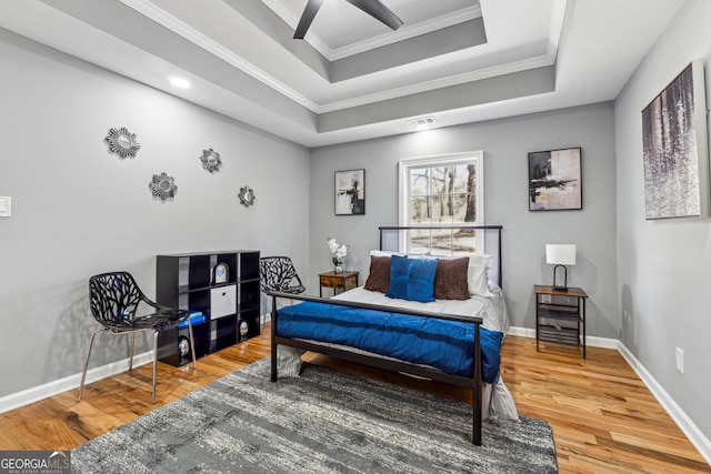 bedroom featuring a tray ceiling, wood finished floors, visible vents, and crown molding