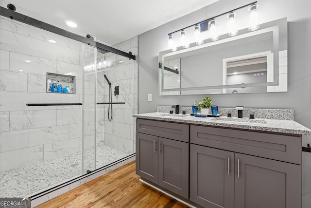 bathroom with a stall shower, double vanity, a sink, and wood finished floors