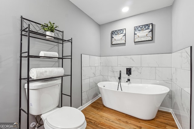 bathroom with tile walls, recessed lighting, a freestanding bath, toilet, and wood finished floors