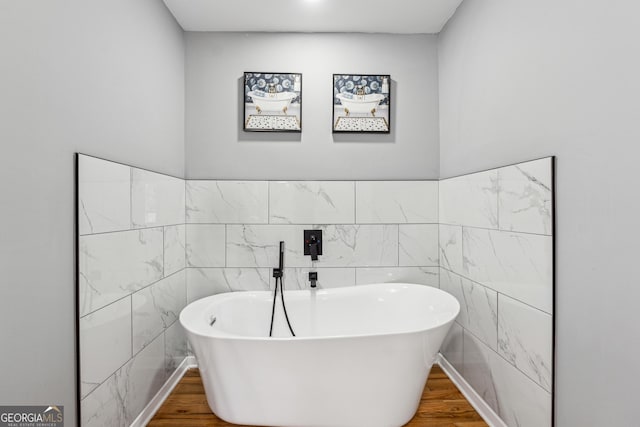 bathroom with wood finished floors, a freestanding tub, and tile walls