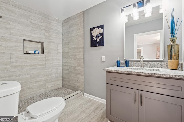 bathroom with toilet, baseboards, a tile shower, and vanity