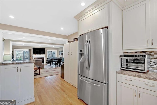 kitchen with stainless steel fridge, tasteful backsplash, open floor plan, light stone countertops, and light wood-style floors