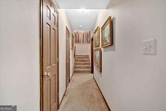 hall featuring light carpet, baseboards, stairway, and a textured ceiling