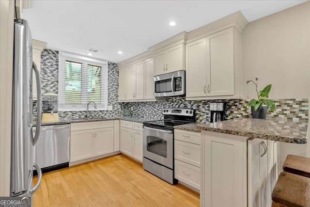 kitchen featuring stainless steel appliances, a sink, light wood-style flooring, and tasteful backsplash