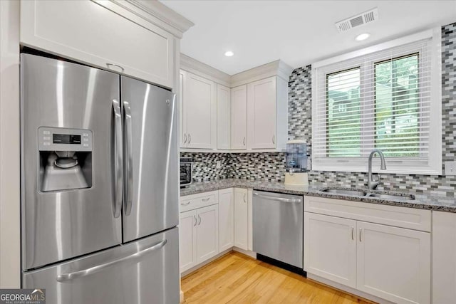 kitchen featuring stainless steel appliances, a sink, visible vents, white cabinetry, and backsplash