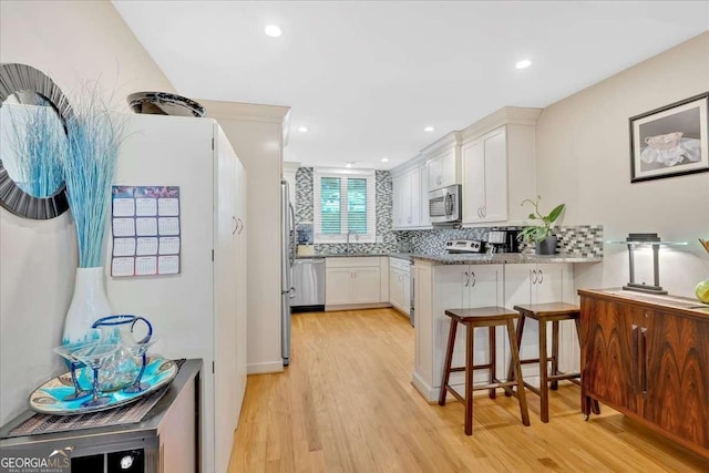 kitchen featuring stainless steel appliances, tasteful backsplash, light wood-type flooring, and a peninsula