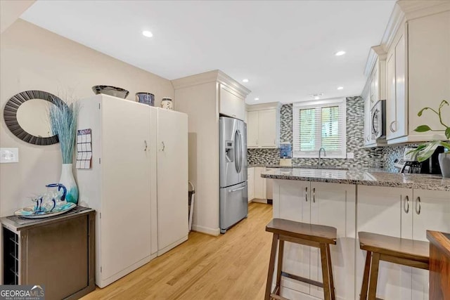 kitchen featuring light stone counters, decorative backsplash, appliances with stainless steel finishes, light wood-style floors, and a peninsula