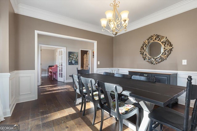 dining area featuring dark wood-style floors, crown molding, a decorative wall, an inviting chandelier, and wainscoting