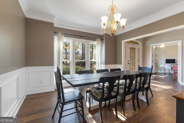 dining space with dark wood-type flooring, wainscoting, crown molding, and a notable chandelier